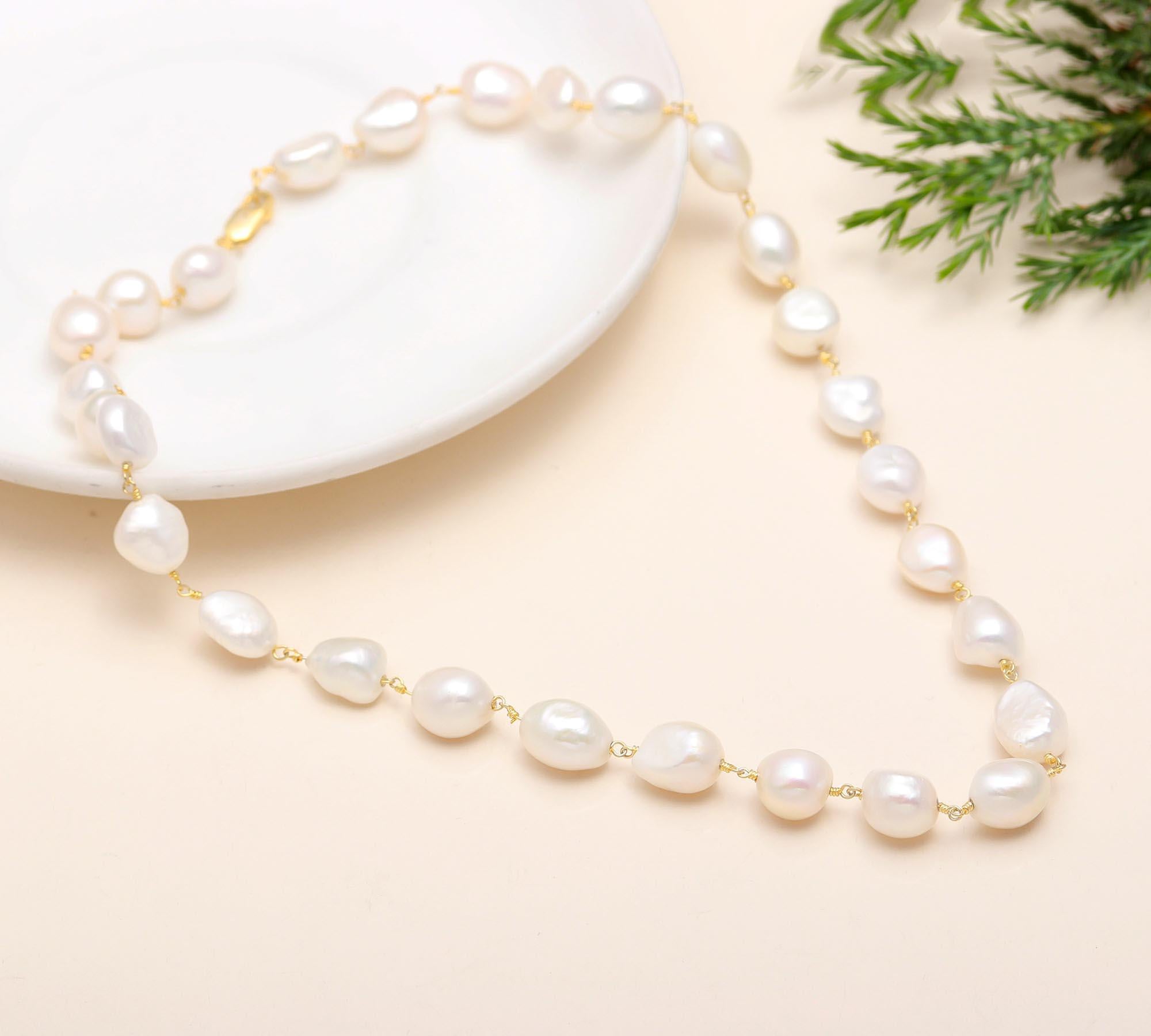 Pearl necklace on a beige surface with a white dish and greenery in the background