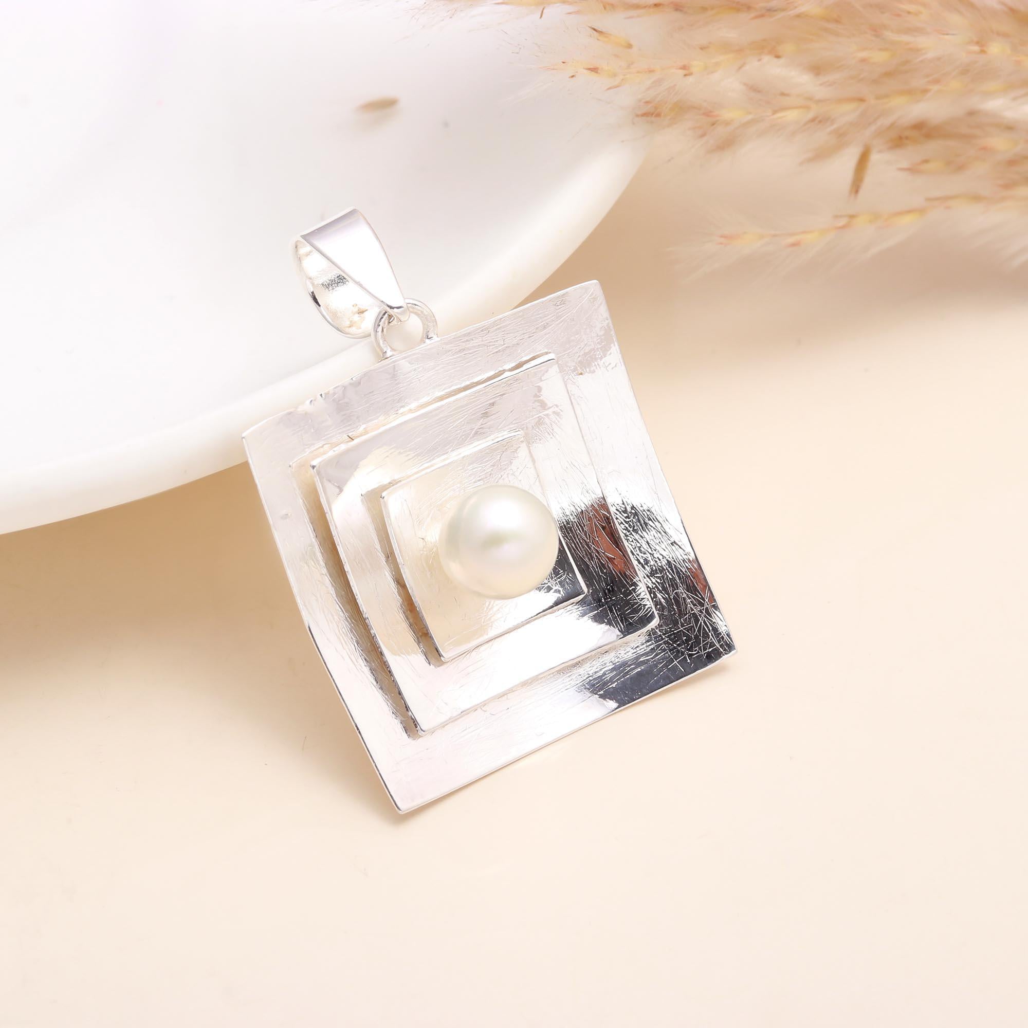Sterling silver geometric pendant with white pearl centerpiece on a hand, modern square design.