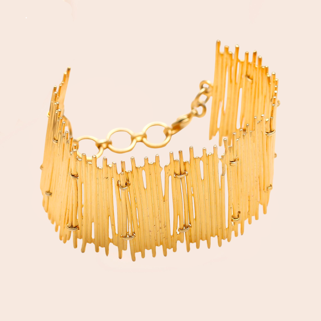 Gold statement bracelet on a light pink background